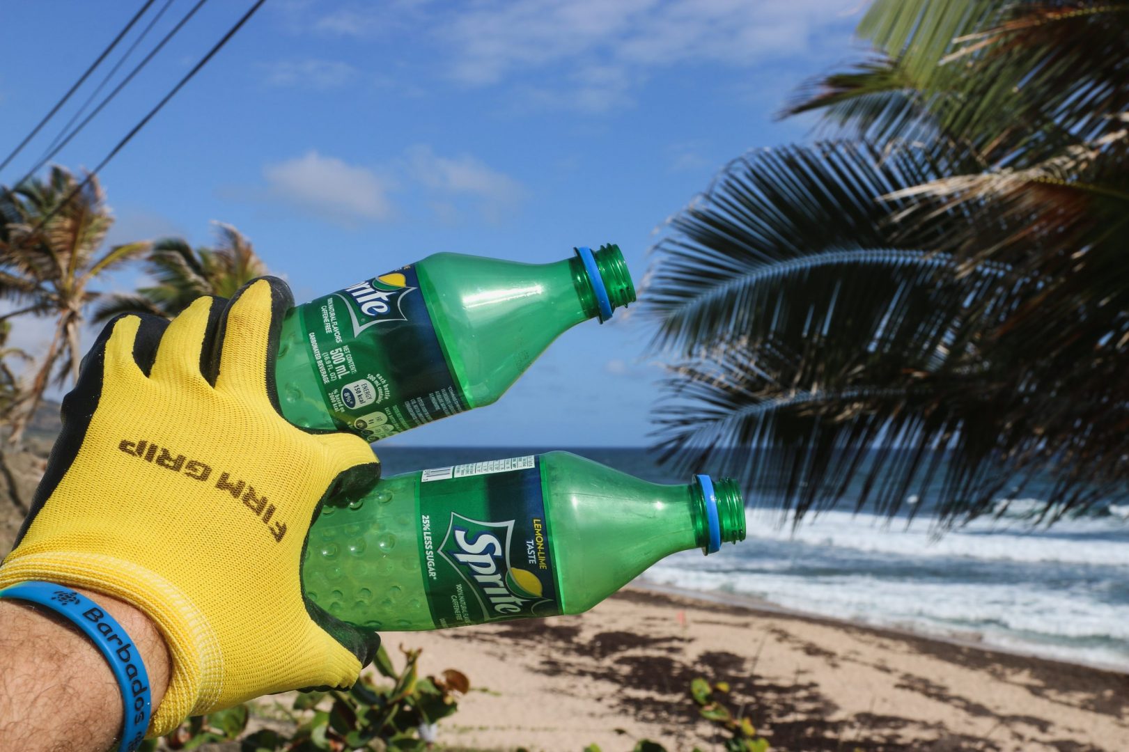 person in yellow glove holding two Sprite plastic bottles